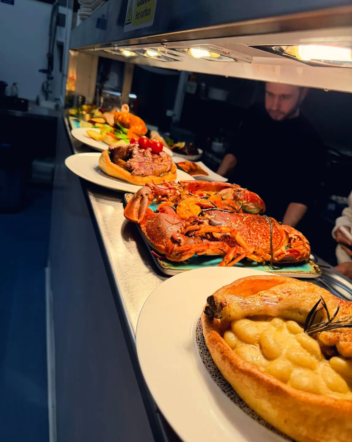 The chef at the pass with plates lined up under the lamps
