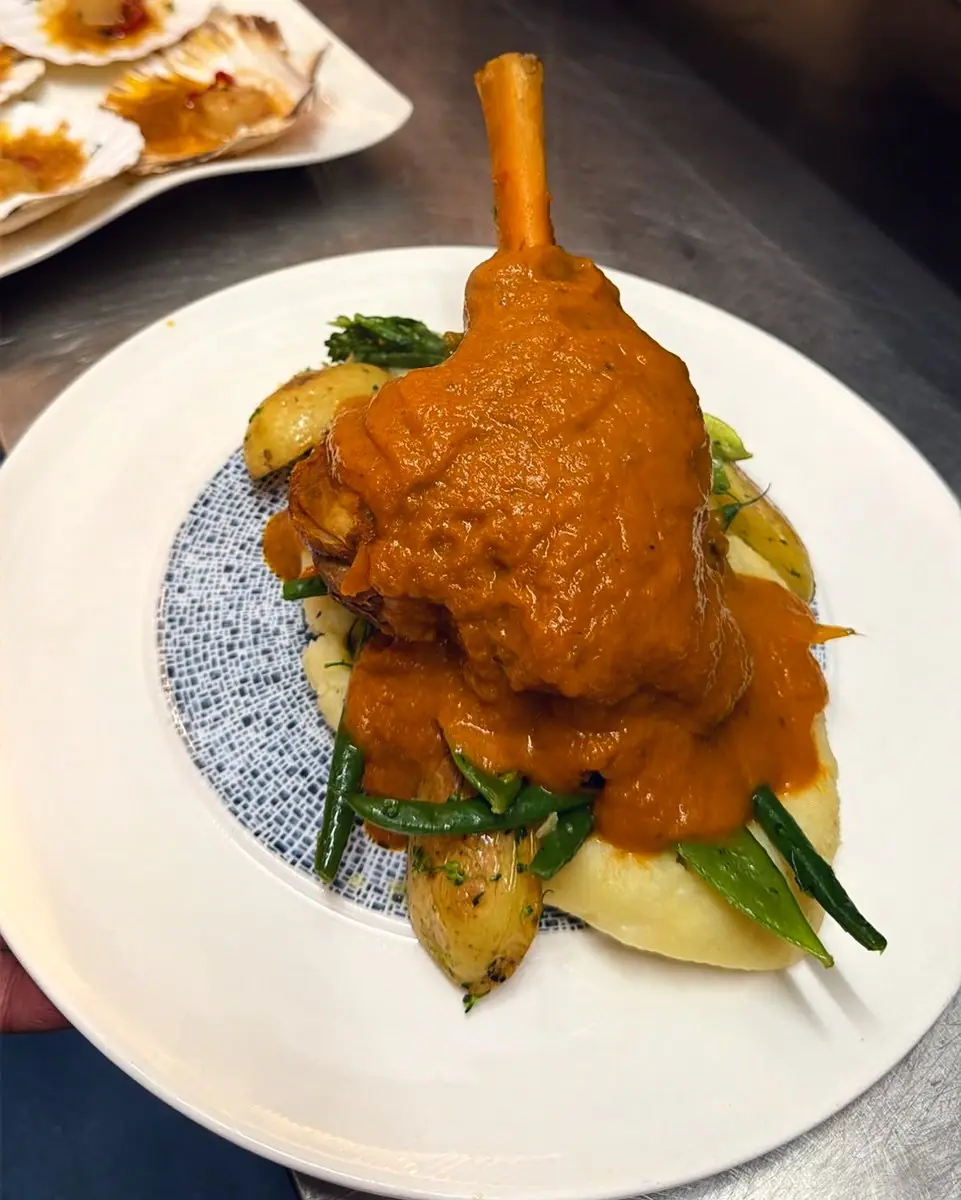 A lamb shank in a rich sauce over mash and green beans