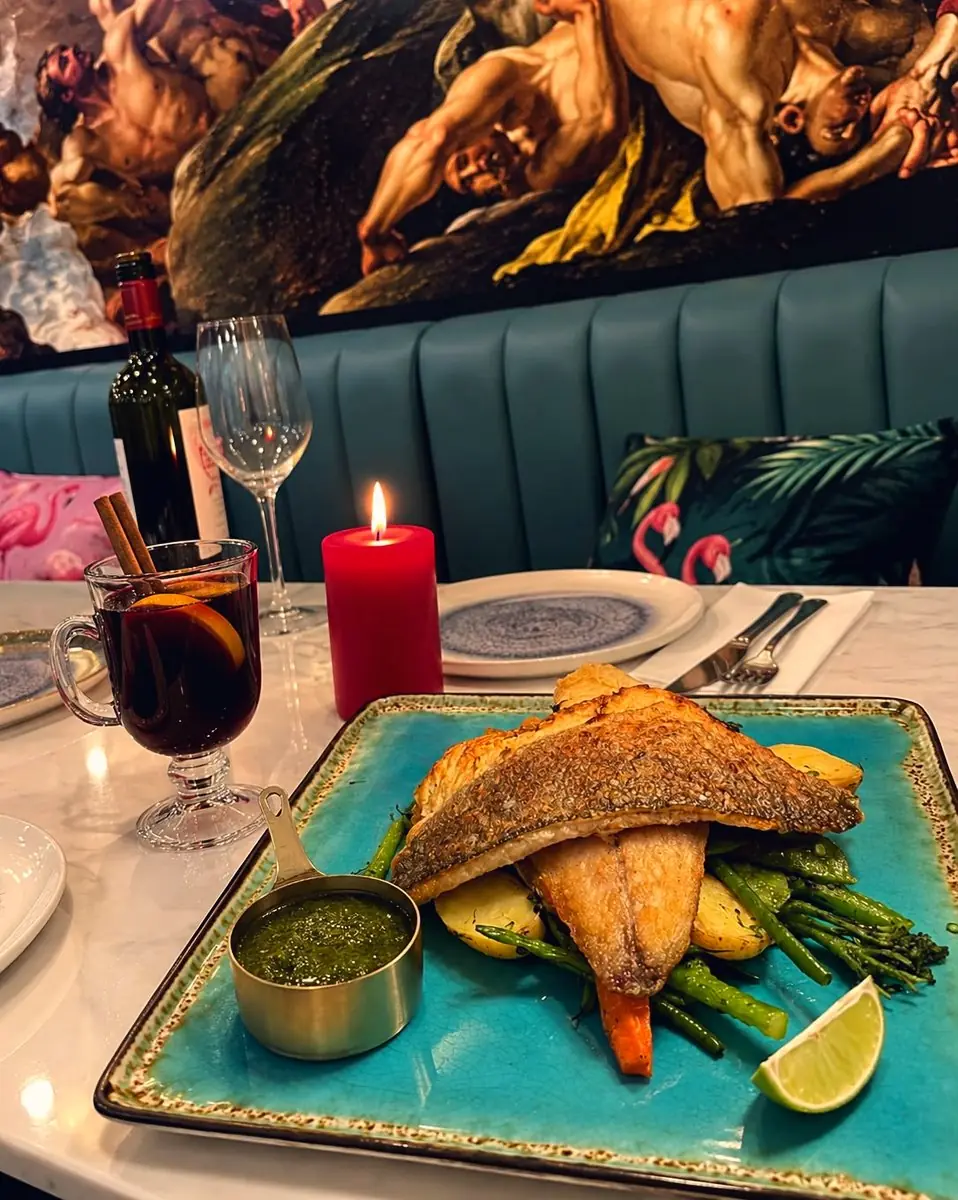 Fish on a turquoise plate with greens and lime, a red candle and mulled wine behind it