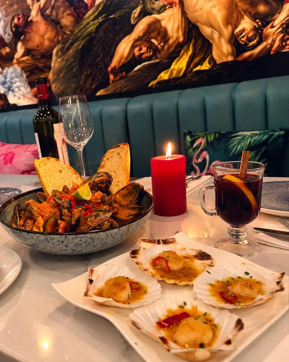 A candlelit table under the painted sky, scallops in their shells and mulled wine